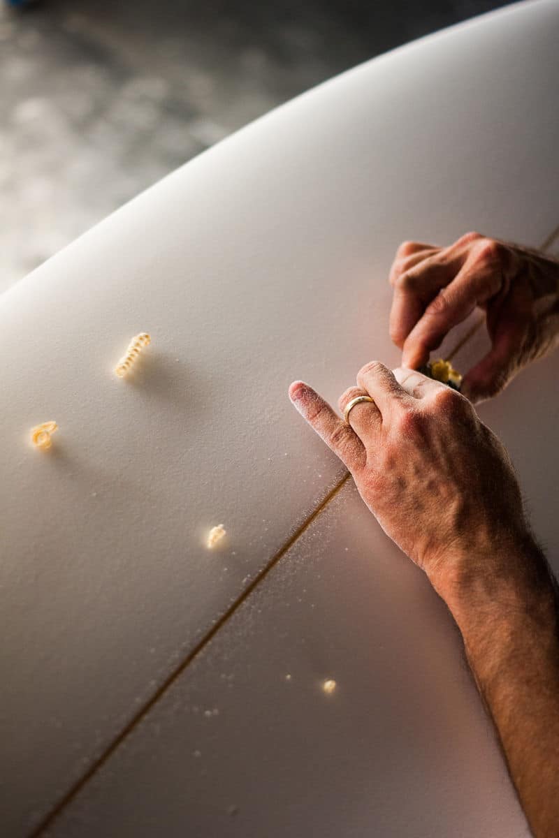 Shapers-Club- Un homme met de la cire sur une planche de surf. -surfshop-surfboard