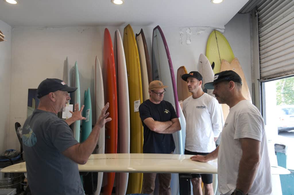 Shapers-Club- Four men discussing Gordon Smith surfboards in a surf store. -surfshop-surfboard
