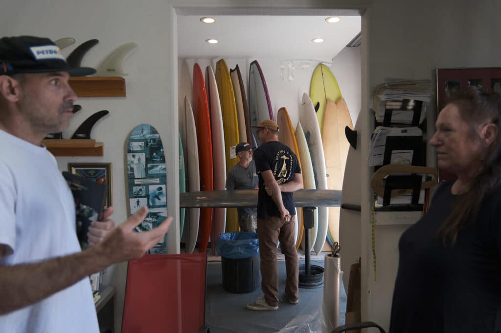 Shapers-Club- People conversing in a surf shop surrounded by colorful surfboards. -surfshop-surfboard