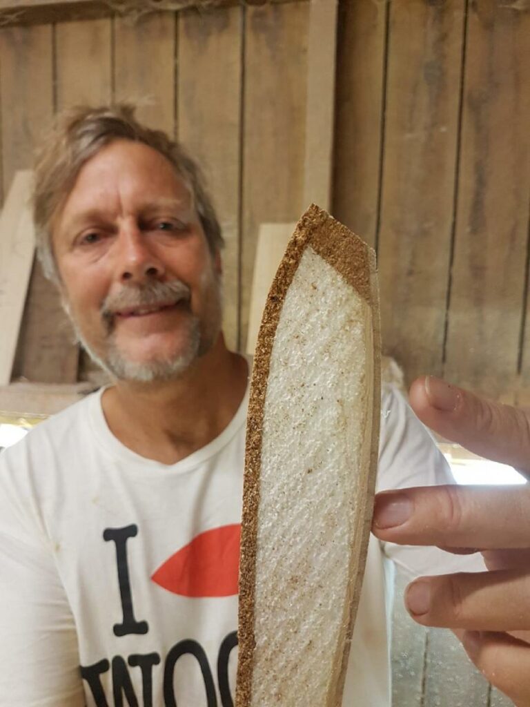 Shapers-Club- Smiling man behind a slice of bread with an unusually thick crust, influenced by cultural influences. -surfshop-surfboard