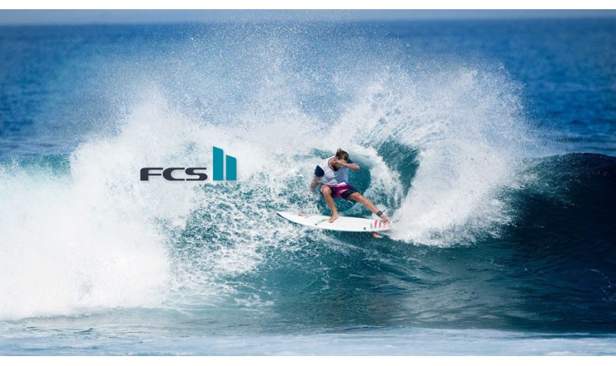 Shapers-Club- Un surfeur surfant sur une grosse vague, avec un jet d'eau dynamique autour de lui. le surfeur est accroupi sur une planche de surf blanche, marquée du logo fcs. -surfshop-surfboard