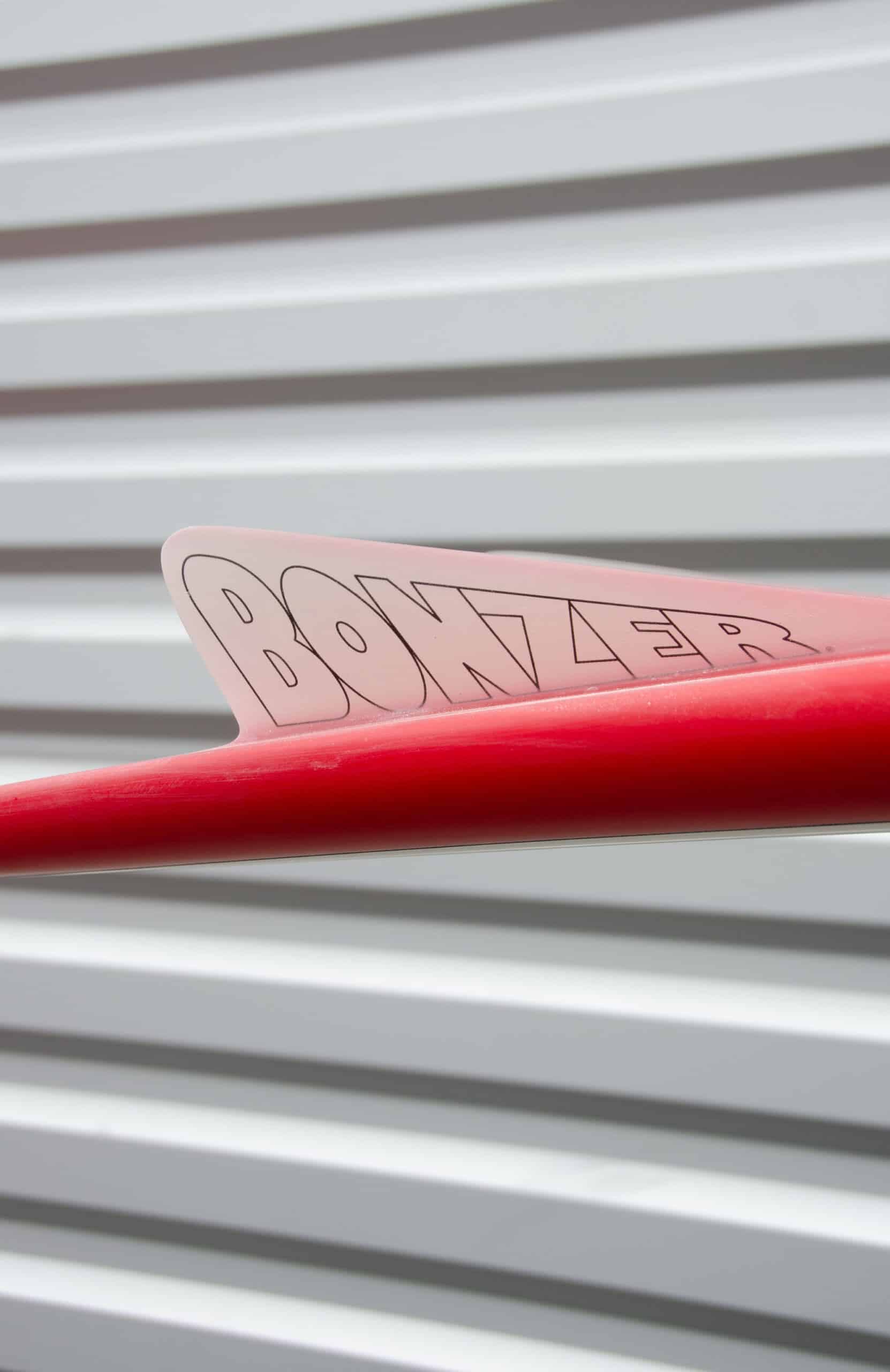 Shapers-Club- Close-up of a Russ Short 6'2" x 19' 1/2" x 2' 1/2" red surfboard fin labeled "BONZER", set on a white horizontal cover. -surfshop-surfboard